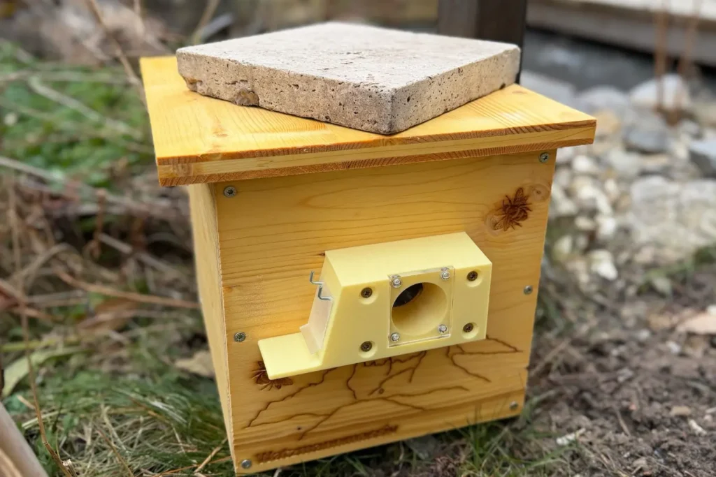 Aufgestellter Hummelkasten im Garten, dessen Dach im Spätwinter mit einem Stein gegen Wind beschwert ist