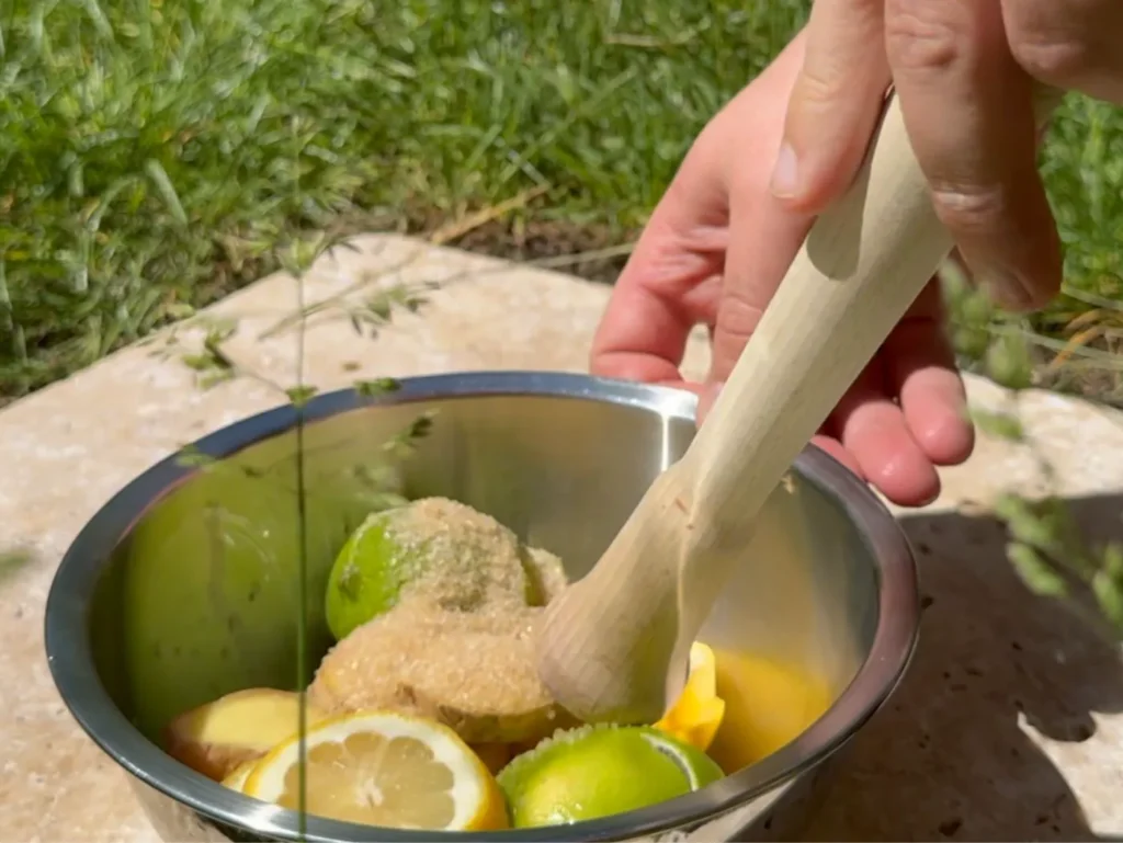 Schüssel mit Ingwer, Limette, Zitrone und Zucker. Zutaten werden mit Stößel zerdrückt.