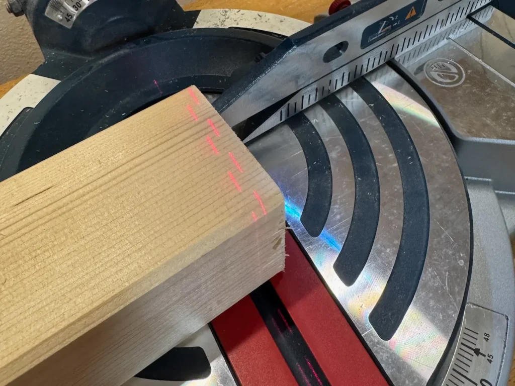 Kantholz liegt auf einer Kappsäge. Ein Laser zeigt den Schnitt an.