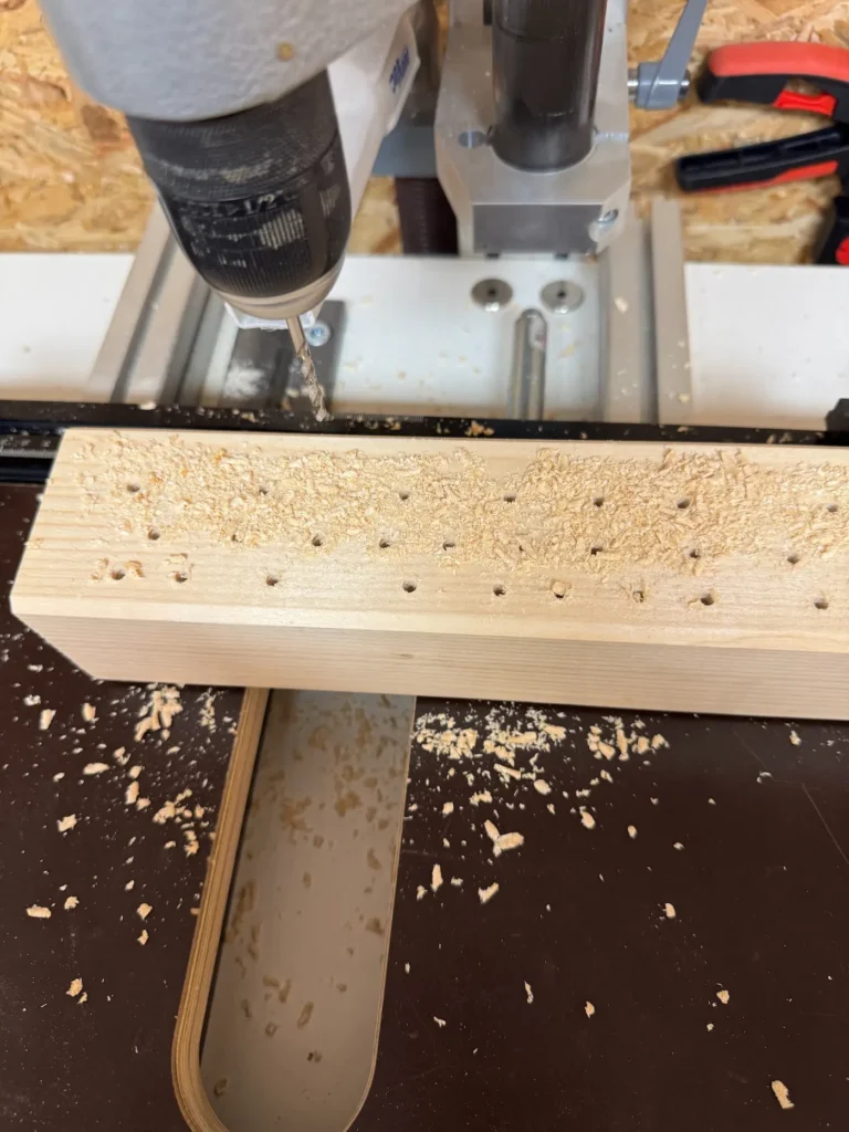 Mehrere Löcher werden mit einer Standbohrmaschine in ein Kantholz gebohrt.