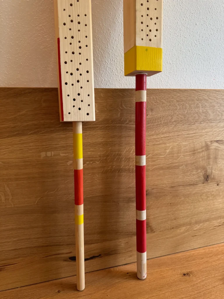 Zwei bunt angemalte Nisthilfen sehen im Wohnzimmer auf einer Sitzbank.
