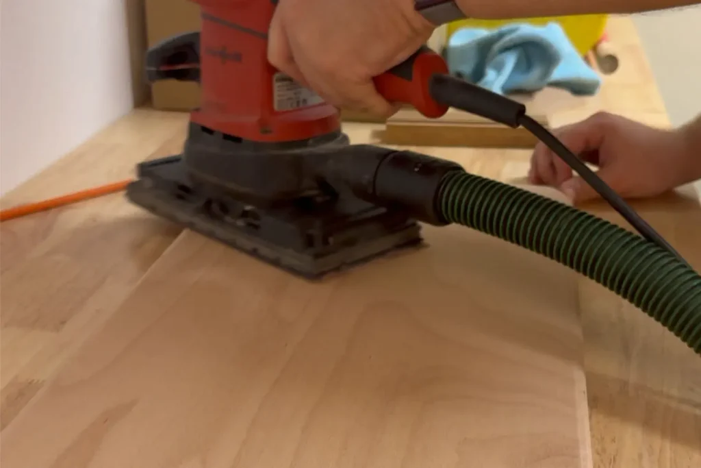 Eine Holzplatte wird mit einem Schwingschleifer geschliffen.