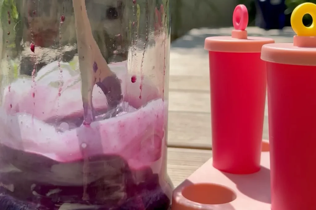 Glasbehälter mit Blaubeer-Sahne-Masse und zwei Eisformen stehen auf einem Holzsteg im Garten.