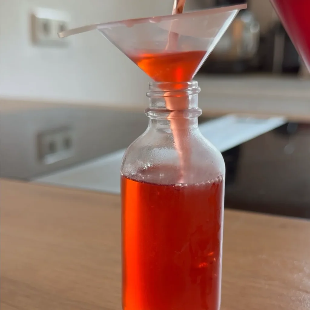 Eine kleine Flasche mit Erdbeersirup und einem Trichter zum Einfüllen.