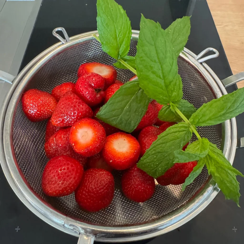 Frische Erdbeeren und Minze in einem Sieb.