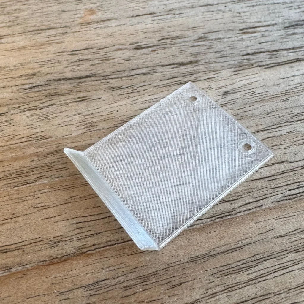 Nahaufnahme der gedruckten transparenten Wachsmottenklappe aus PLA, liegend auf einer Holzoberfläche.