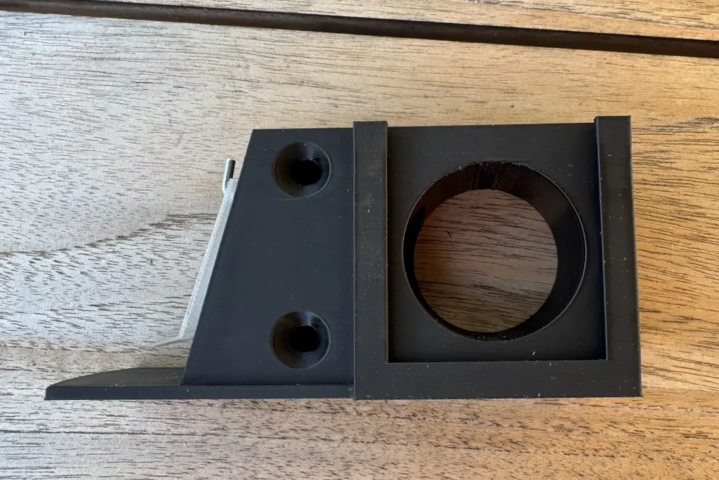 Seitenansicht schwarzer Vorbau mit montierter transparenter Klappe, befestigt mit zwei kleinen L-Haken.