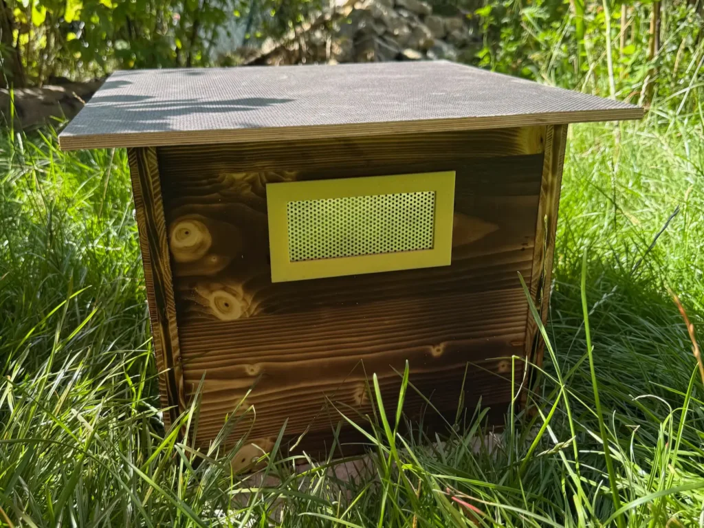 Hummelkasten mit Lüftungsgitter aus Edelstahl in einem gelbem Lüftungsrahmen