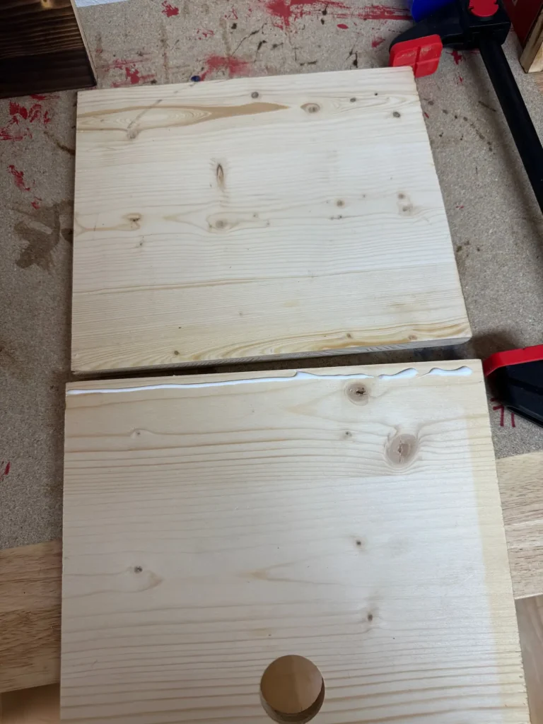 zwei helle Holzplatten mit Bohrungen liegen auf einer Werkbank, eine Platte ist mit Holzleim an der Kante versehen.
