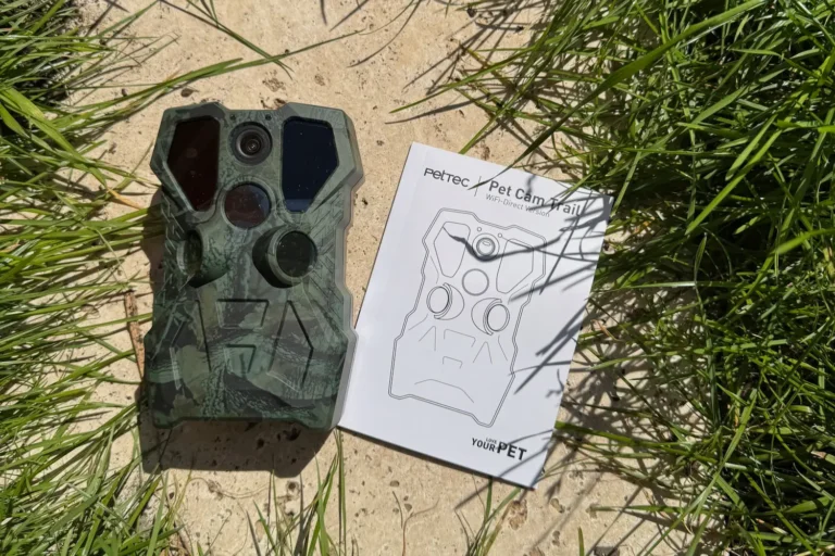 Wildtierkamera PetTec Cam Trail im Test: Nachts im Garten auf Entdeckungstour PetTec Pet Cam Trail Wildkamera im Tarngehäuse neben der Bedienungsanleitung auf Steinboden mit Gras.
