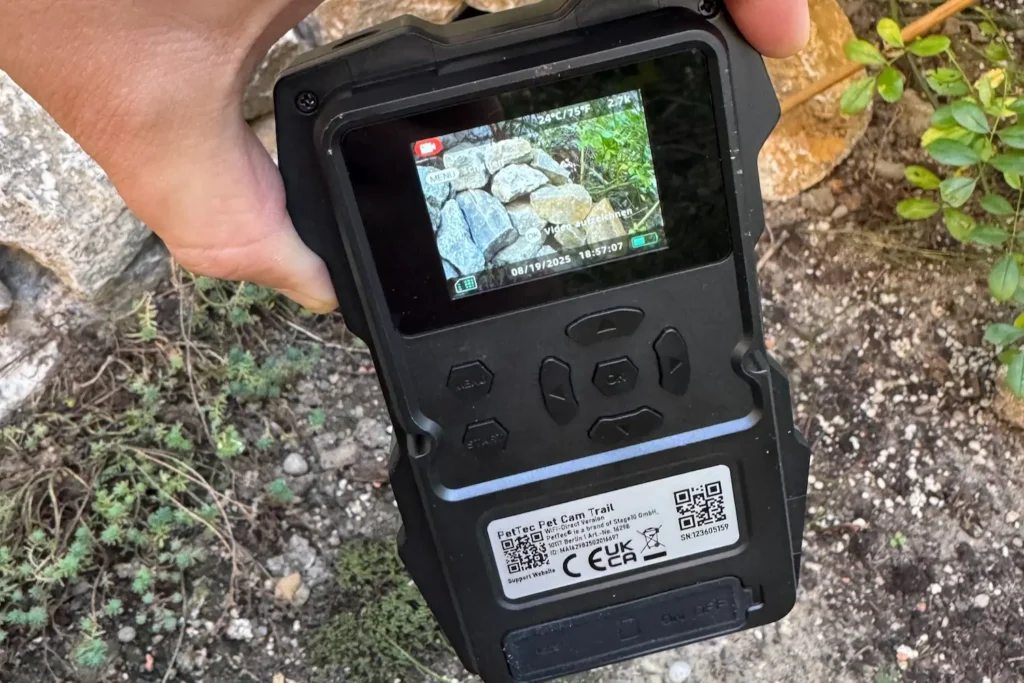 Rückseite der PetTec Pet Cam Trail mit Display, das eine Videoaufnahme von Steinen und Pflanzen anzeigt.