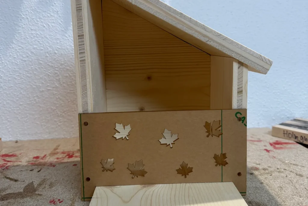 Eichhörnchen-Futterhaus im Rohbau mit dekorativer Frontplatte und Blattausschnitten.
