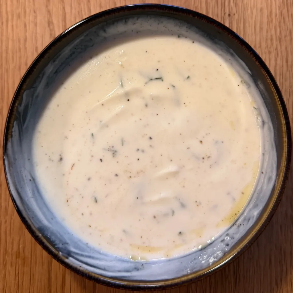 Schüssel mit cremigem Joghurt-Minz-Dip, gewürzt mit Olivenöl, Salz und Pfeffer.