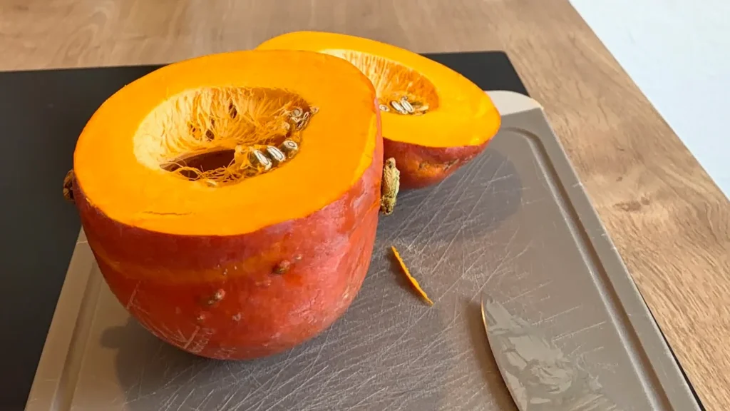 Halbierter Hokkaido-Kürbis mit leuchtend orangefarbenem Fruchtfleisch auf einem Schneidebrett.