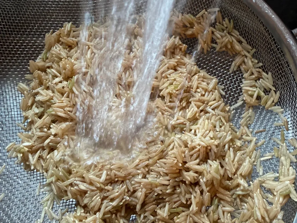 Basmati-Reis wird in einem feinen Sieb unter fließendem Wasser gespült.