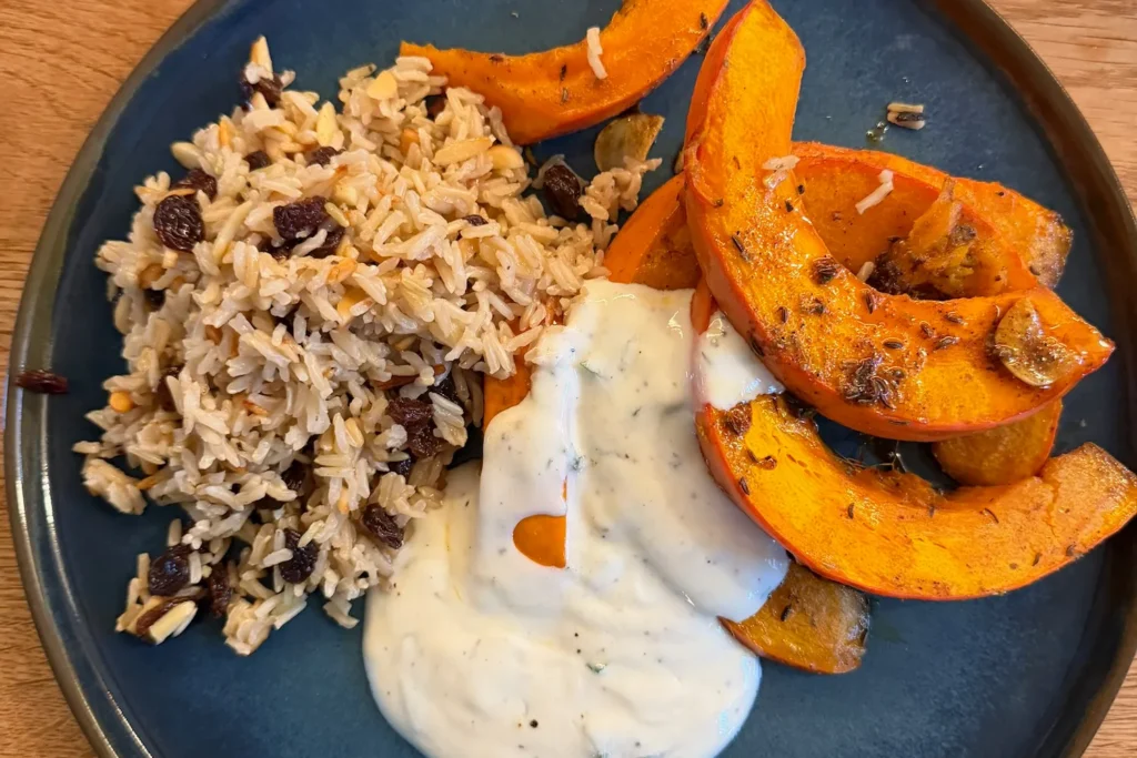 Teller mit Ofenkürbis, orientalischem Reis mit Rosinen und Mandeln sowie cremigem Joghurt-Dip.