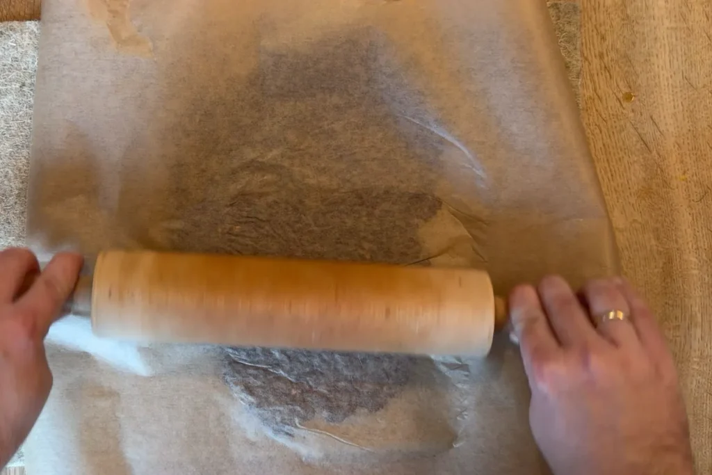 Papiermasse wird zwischen Backpapier mit einem Nudelholz ausgerollt.