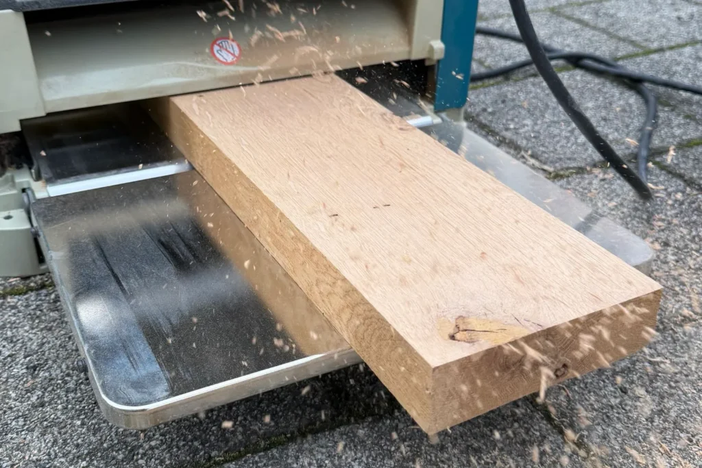 Eichenbretter werden mit einer Dickenhobelmaschine für den Kratzstamm plan gehobelt.