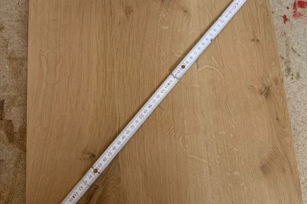 Mit einem Meterstab wird diagonal die Mitte der Eichenplatte für den Kratzstamm ermittelt.