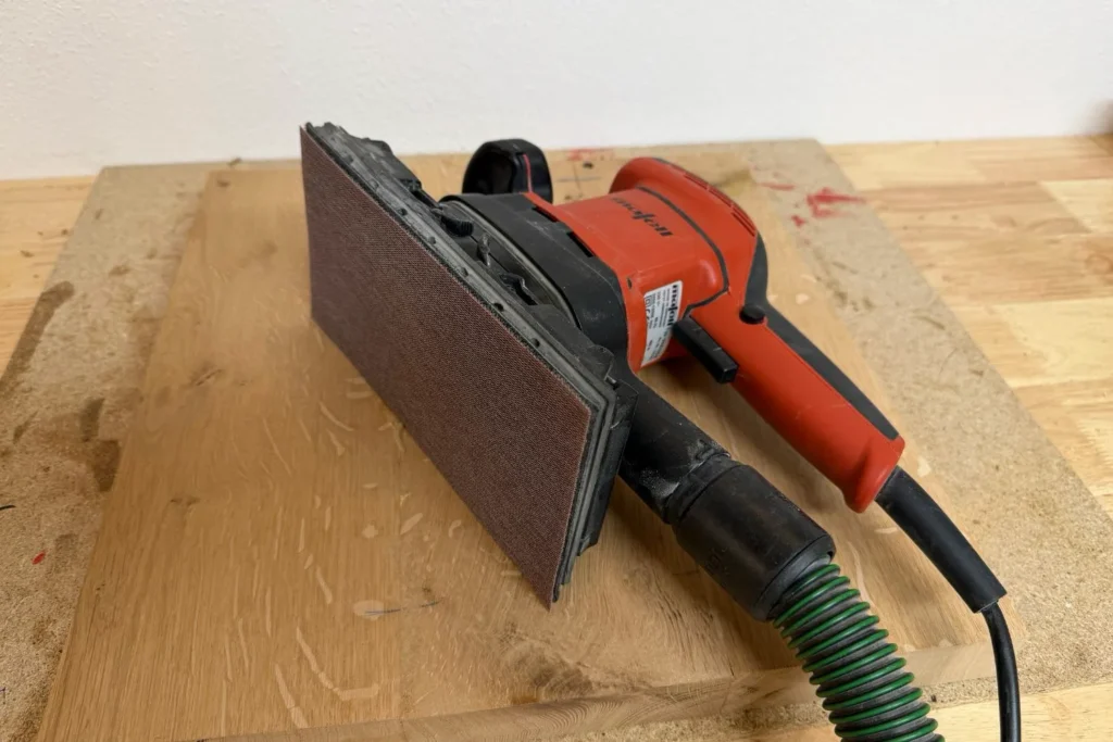 Schwingschleifer glättet die Oberfläche der Eichen-Bodenplatte für den DIY-Kratzstamm.