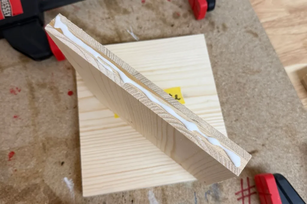 Leim wird auf die Kante des Seitenteils aufgetragen, bevor es mit der Rückwand verbunden wird.