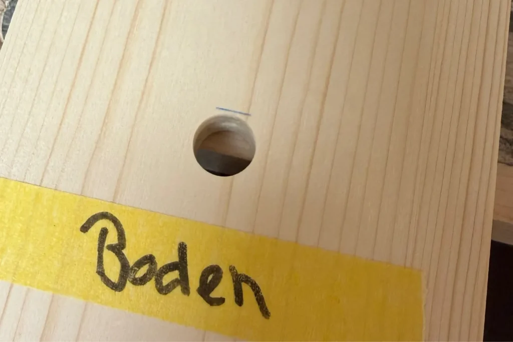 Fertig gebohrter Wasserablauf in der Bodenplatte des Nistkastens, gekennzeichnet mit gelbem Klebeband.