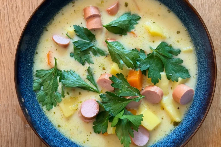 Herzhafte Kartoffelsuppe mit Karotten, Lauch und Speck Teller mit stückiger Kartoffelsuppe, Wiener Würstchen und frischer Petersilie in einer blauen Schale