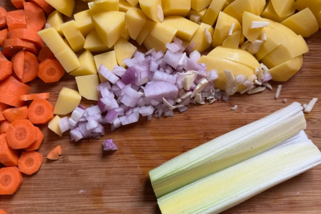 Geschnittene Karotten, Kartoffeln, Zwiebeln und Lauch auf einem Holzbrett, vorbereitet für die Kartoffelsuppe