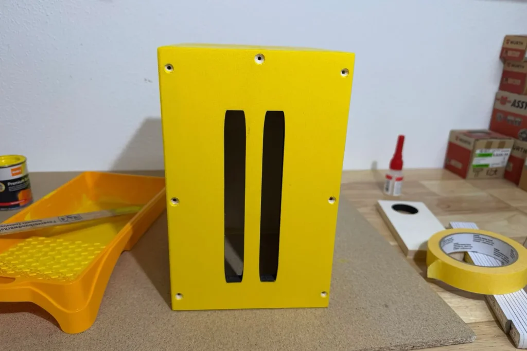 Gelb gestrichene Vorderseite eines Schmetterlingshauses mit zwei Einflugschlitzen.