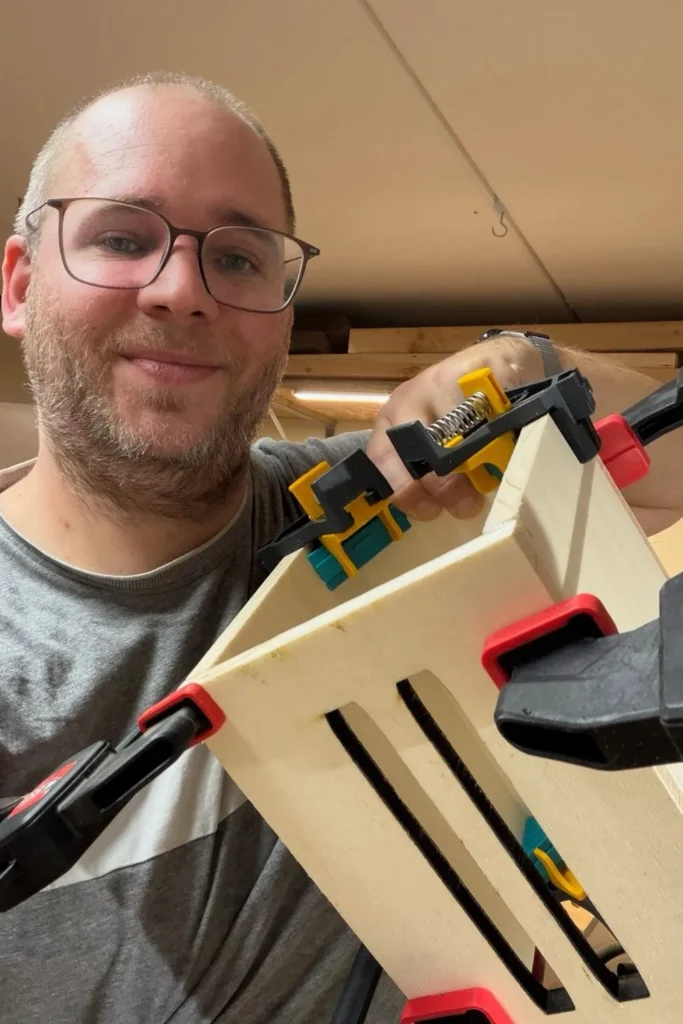 Selfie von Mann mit Schmetterlingshaus, das frisch verleimt und von Zwingen zusammengehalten wird.