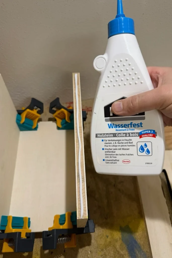 Holzleim wird auf die Kante einer Seitenwand eines Schmetterlingshauses aufgetragen.