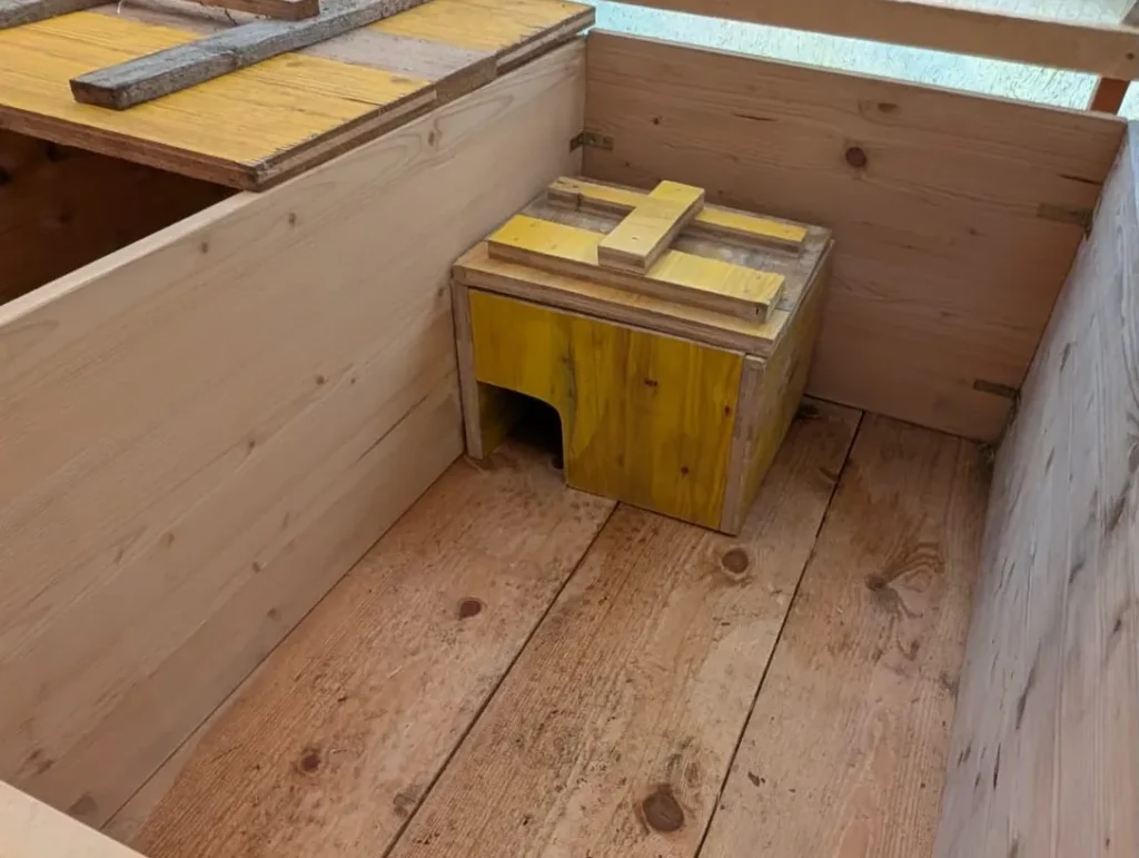 Kleines gelbes Igelhaus aus Holz im Inneren eines größeren Überwinterungsgeheges.