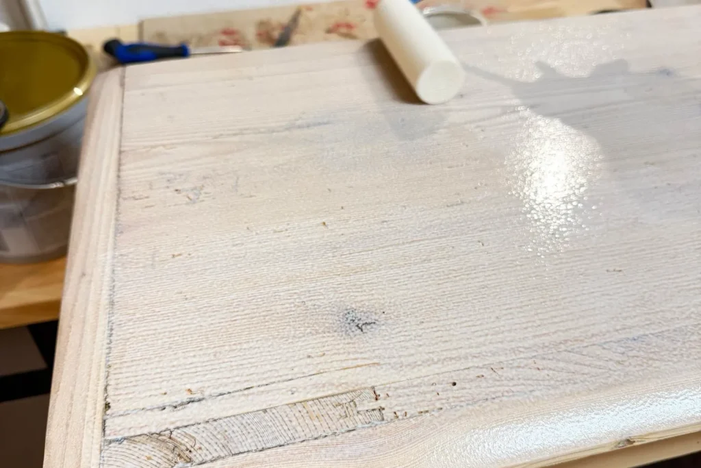 Kalkweiße Holzlasur wird mit einer Lackwalze dünn aufgetragen.