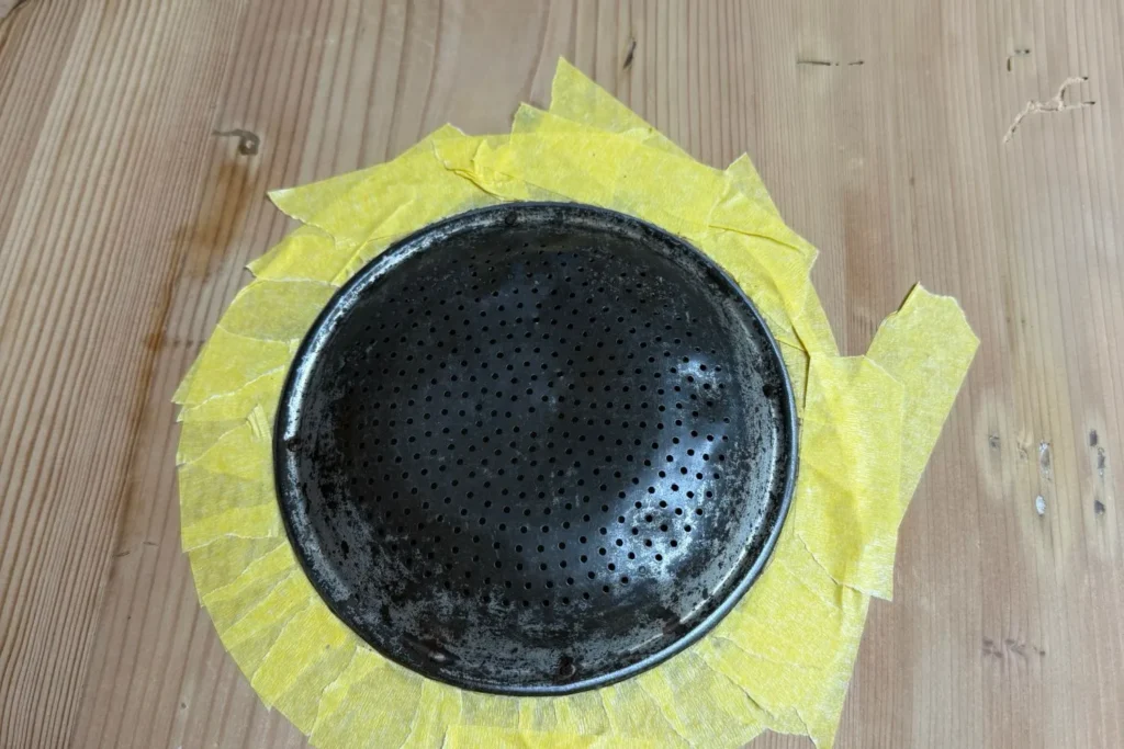 Das runde Lüftungsgitter des Brotschranks wird vor dem Lackieren sorgfältig abgeklebt.