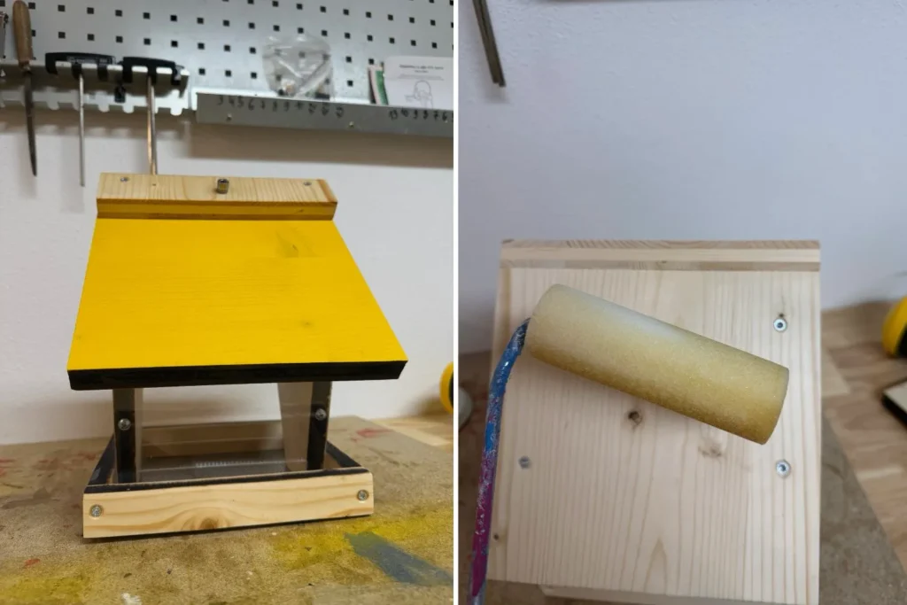 Selbstgebautes Vogelfutterhaus mit gelb lackiertem Dach, daneben Farbrolle beim Anstrich