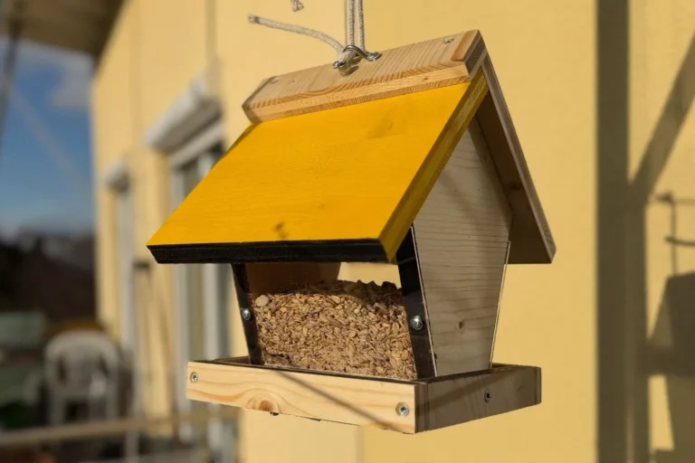 Vogelfutterhaus selber bauen – einfache DIY-Anleitung mit Gitterboden Selbstgebautes Vogelfutterhaus mit gelbem Dach aufgehängt auf dem Balkon.
