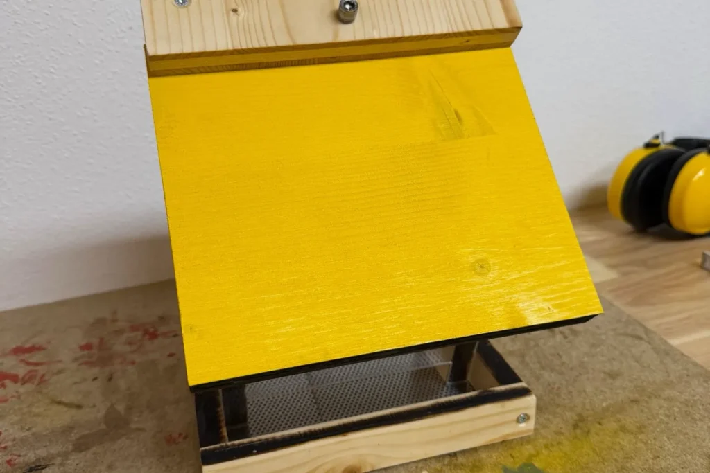 Selbstgebautes Vogelfutterhaus mit gelb lackiertem Dach.