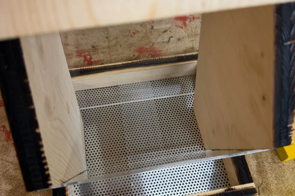 Innenansicht des Vogelfutterhauses: Lochblechboden unter den Seitenteilen, Drainagefunktion sichtbar.