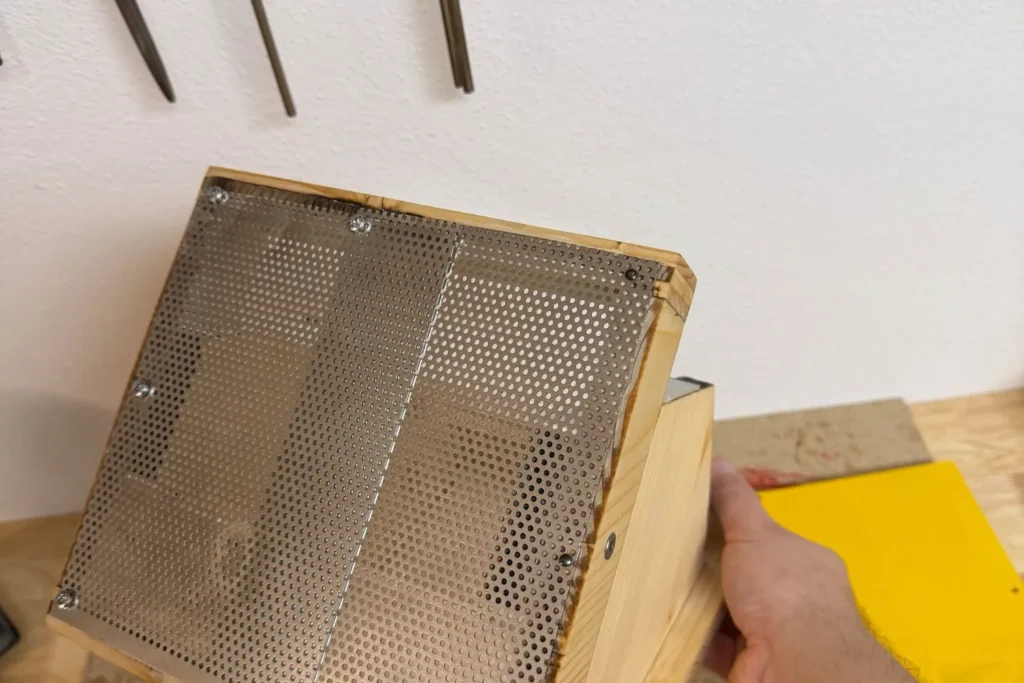 Unterseite des Vogelfutterhauses mit verschraubtem Lochblech als Drainageboden.