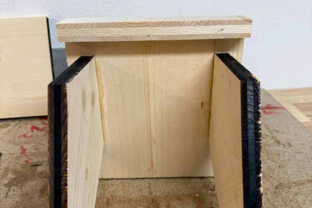 Holz-Vogelfutterhaus während des Aufbaus: Zwei Seitenteile sind innen versetzt unter einer Dachplatte montiert.