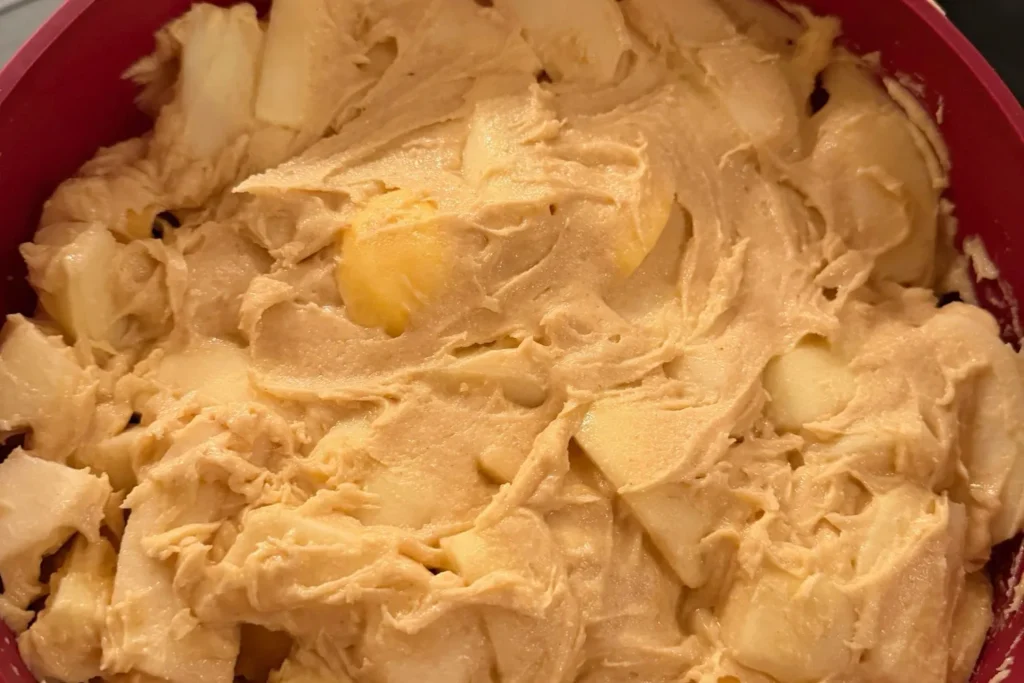 Apfelstücke im fertigen Kuchenteig, kurz bevor der Apfelkuchen gebacken wird.