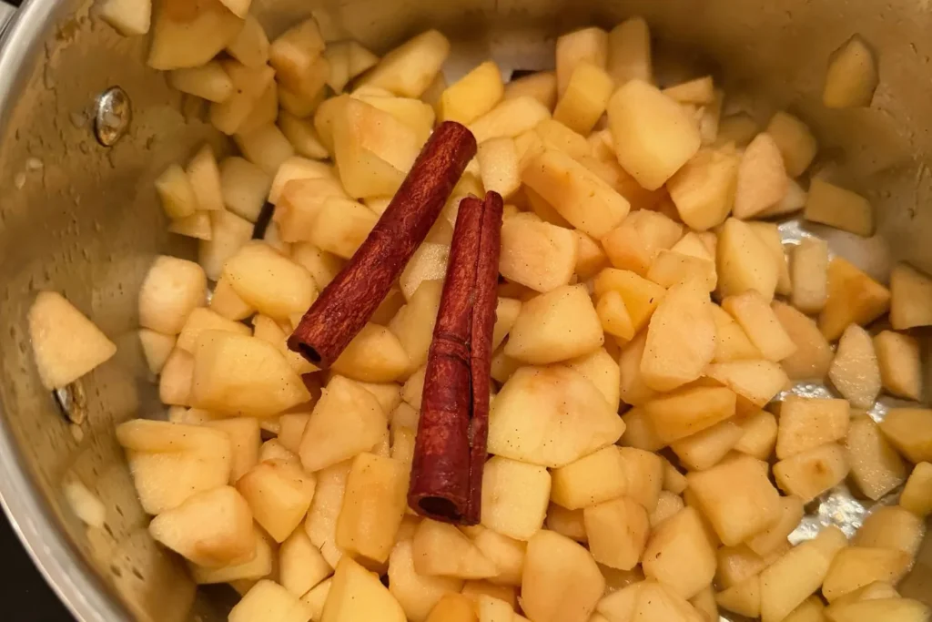 Apfelstücke mit Zimtstangen im Topf – die Basis für ein natürlich süßes Apfelkompott.