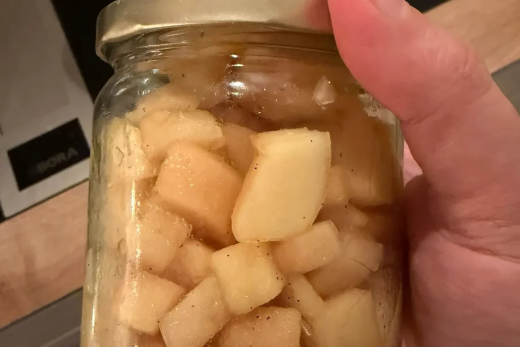 Frisch eingefülltes Apfelkompott im Glas, gehalten in der Hand, kurz nach dem Abfüllen.