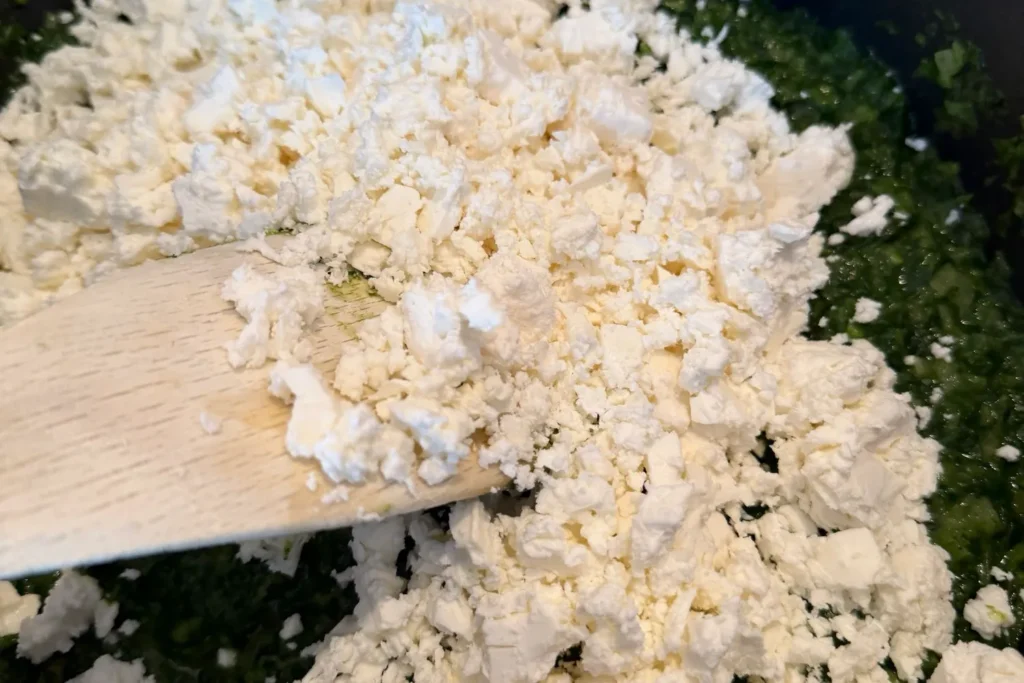Zerbröselter Feta wird unter die Spinatmasse gemischt – klassische Füllung für Börek.