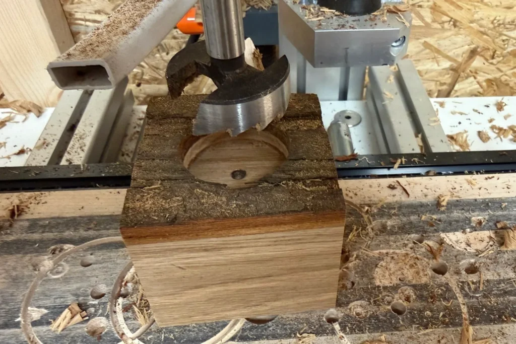 Forstnerbohrer bohrt die Teelichtmulde in einen Eichenwürfel mit Rindenoberfläche.