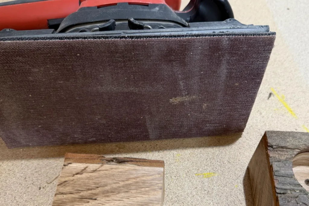 Ein Eichenwürfel liegt vor einem Schleifgerät, die Kanten werden geglättet.