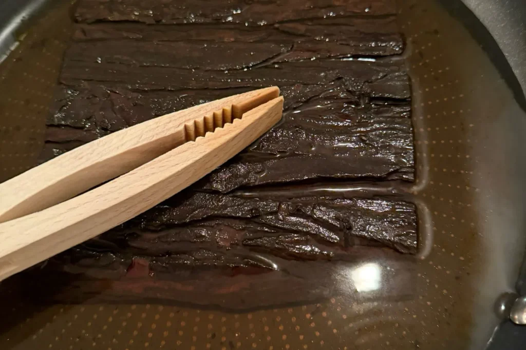 Rindenstücke liegen in einer Pfanne mit Wasser und werden erhitzt, um sie flexibel zu machen.