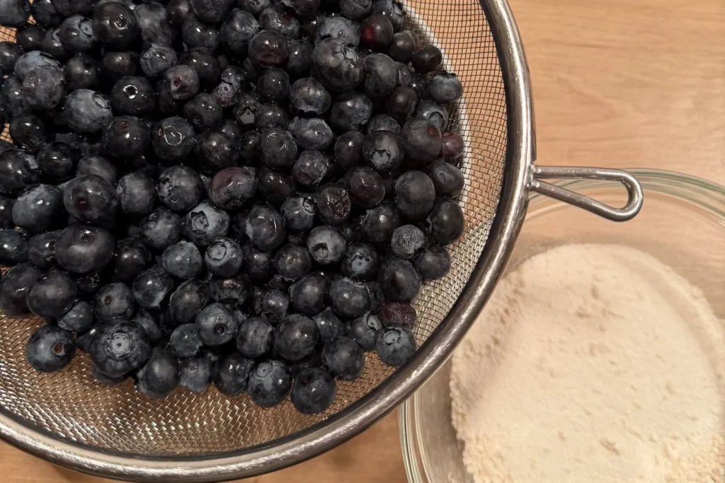 Frisch gewaschene Heidelbeeren liegen in einem Sieb und tropfen über einem Topf ab.