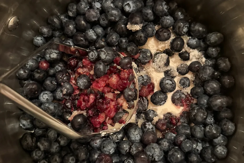 Heidelbeeren werden im Topf leicht zerdrückt, sodass Saft austritt.