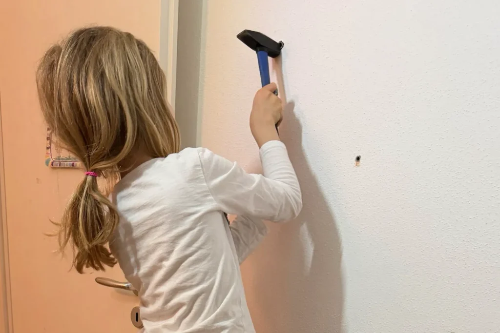 Kind klopft Dübel mit einem Hammer in die Bohrlöcher.